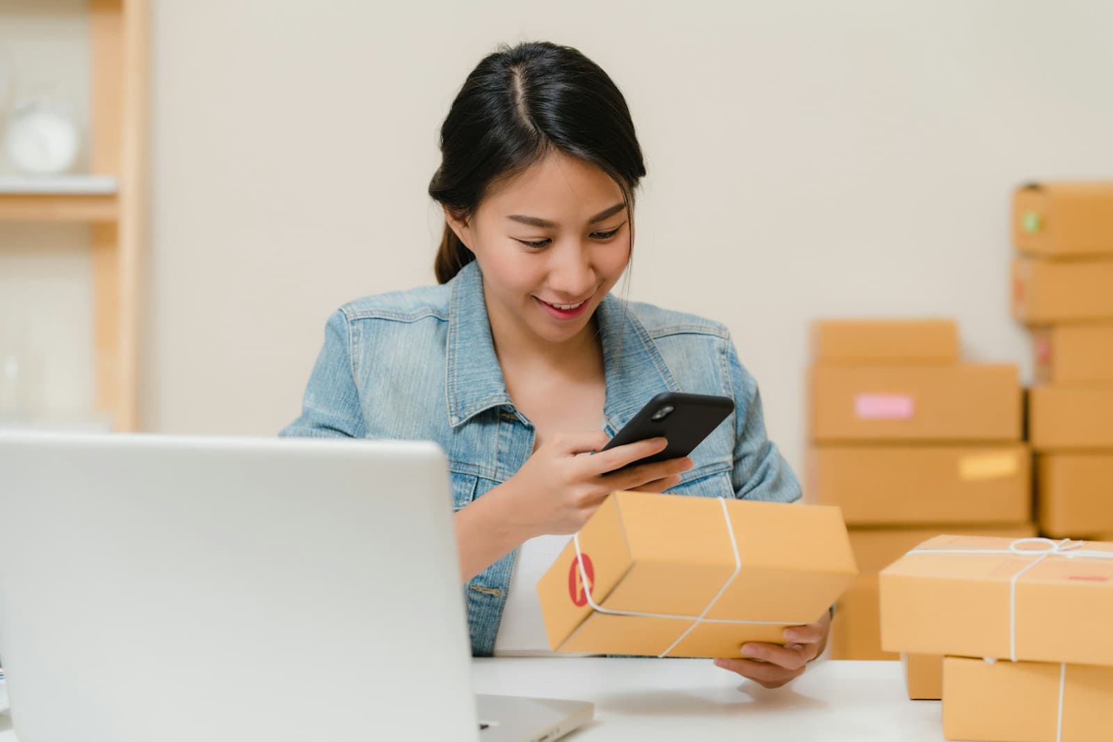 Online seller checking an order on her phone beside parcels